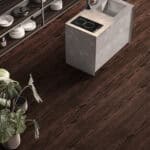 Mountain Lodge Espresso Walnut Wood Look LVT Flooring in a modern kitchen, bringing deep, enveloping warmth with its dramatic, rich tones. This 100% waterproof LVT resists scratches, stains, and dents, offering an effortless to clean, durable foundation for sophisticated comfort.