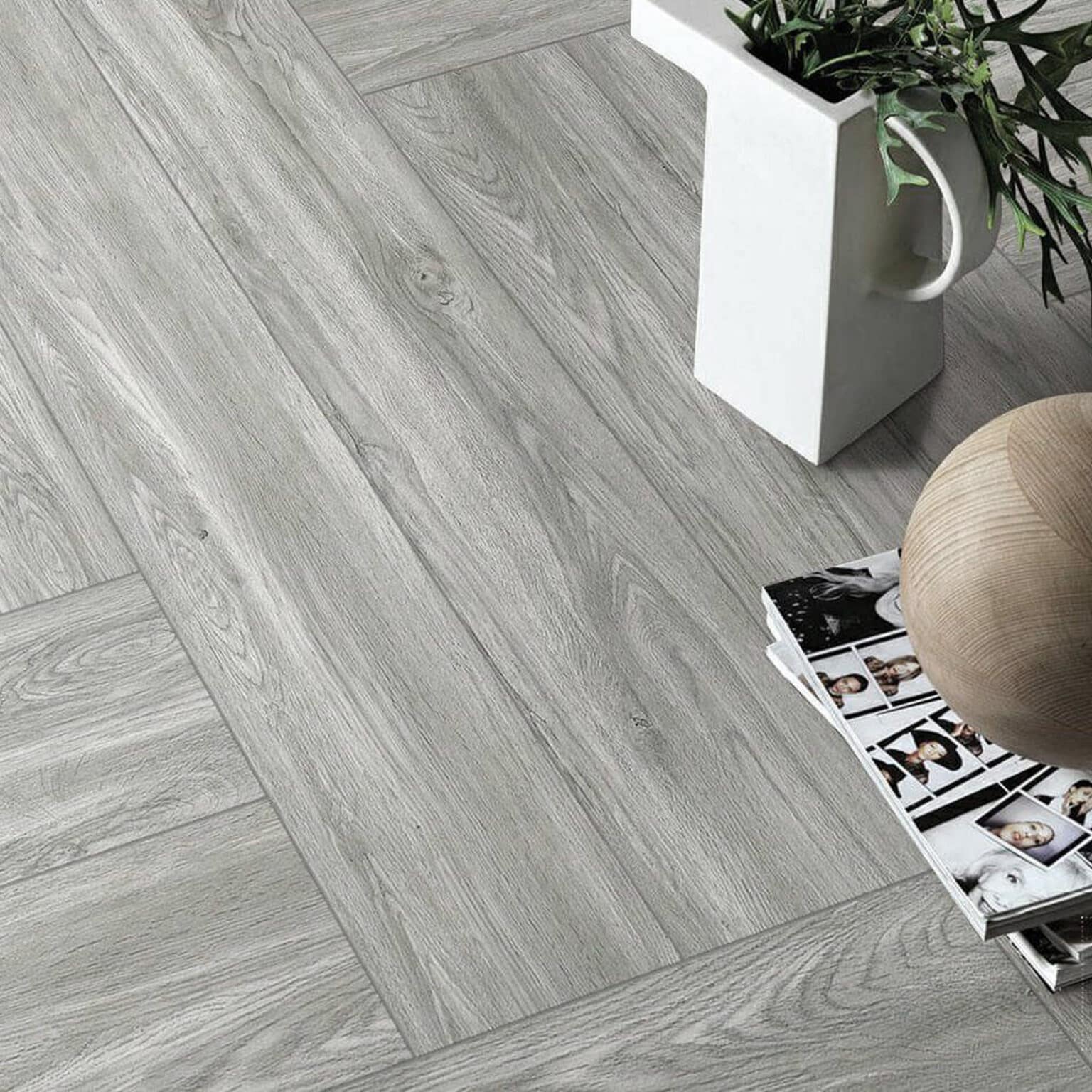 An elegant top-down view of a seating area, where the Effortless Weathered Wood Look Tile acts as a serene, neutral backdrop for two patterned chairs and a small table with white flowers.