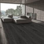 Urban Industrial Graphite Ash Wood Look LVT Flooring in a spacious living room, creating a powerful, sophisticated backdrop with its deep, near-black tones. This 100% waterproof LVT resists scratches, stains, and dents, offering high-impact style for modern industrial lofts.