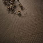 Close-up of Art Deco Cocoa Brown Wood Look Tile on a living room floor, highlighting its intricate pattern and rich cocoa-brown tones. This 100% waterproof porcelain tile offers unmatched durability, resisting scratches and stains for a worry-free, elegant design.