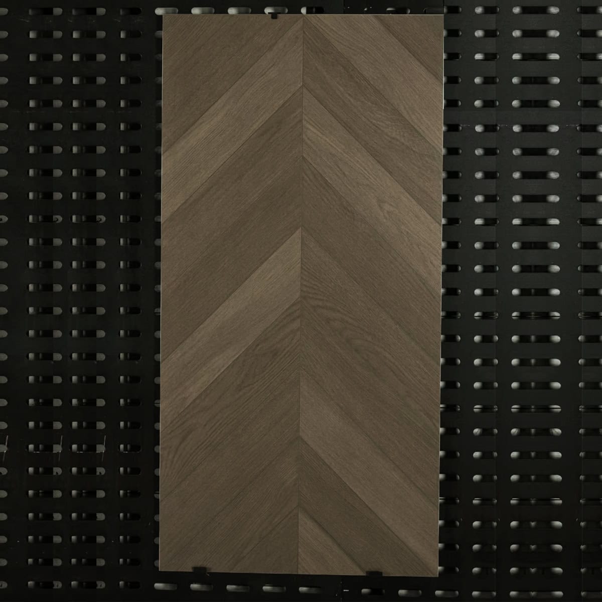 Real photo of a single Italian Minimalism Smoked Brown Wood Look Tile, showcasing its classic chevron pattern and rich, aged-wood texture.