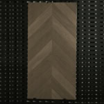 Real photo of a single Italian Minimalism Smoked Brown Wood Look Tile, showcasing its classic chevron pattern and rich, aged-wood texture.
